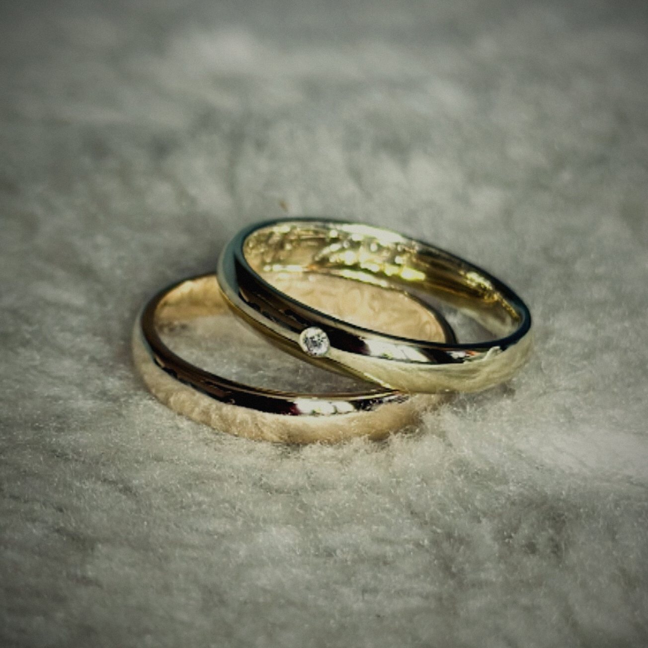 Twee gouden trouwringen, een met een kleine diamant, op een zachte vacht
