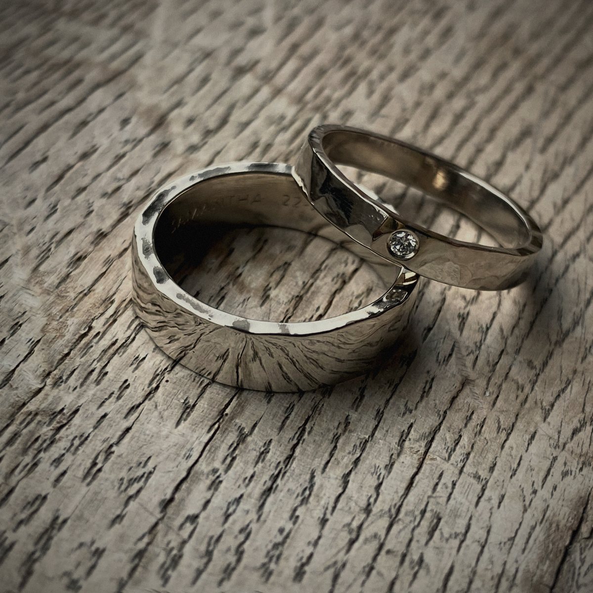 Twee gehamerde zilveren ringen, een met een kleine steen, op eikenhout